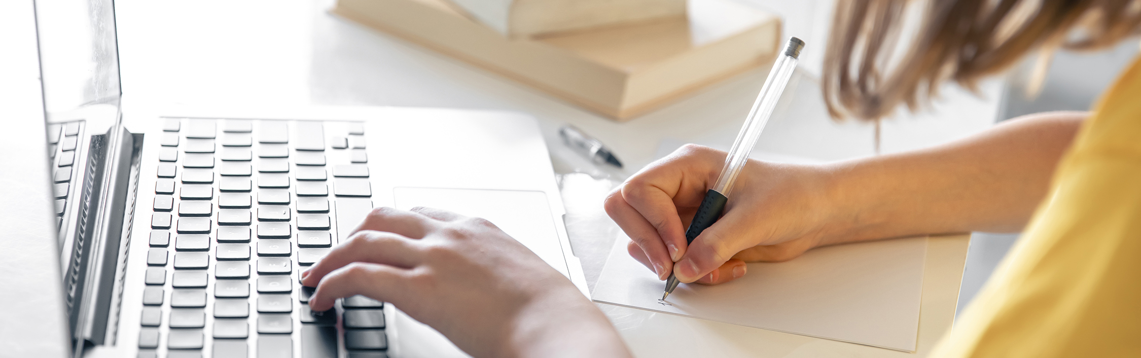 A teenage girl does her homework while sitting with books and a laptop