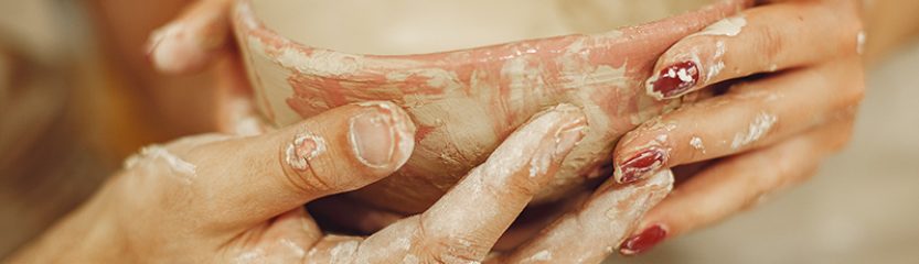 Mutual creative work. Young beautiful couple in casual clothes and aprons. People creating a bowl on a pottery wheel in a clay studio.